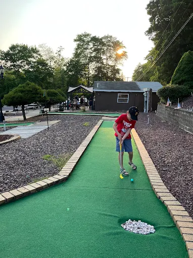 Young guest putting on the mini golf green at sunset